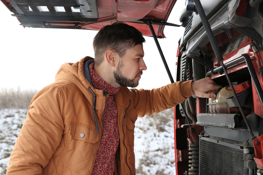 Handsome driver near truck with open hood outdoors