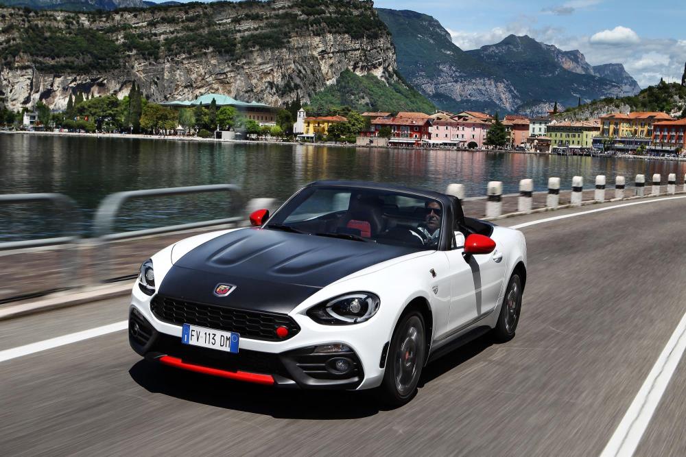 A wonderful Abarth 124 Spider driving along the road next to a lake.